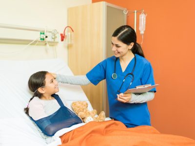 smiling-healthcare-worker-holding-reports-while-looking-little-patient-with-fractured-hand-resting-hospital